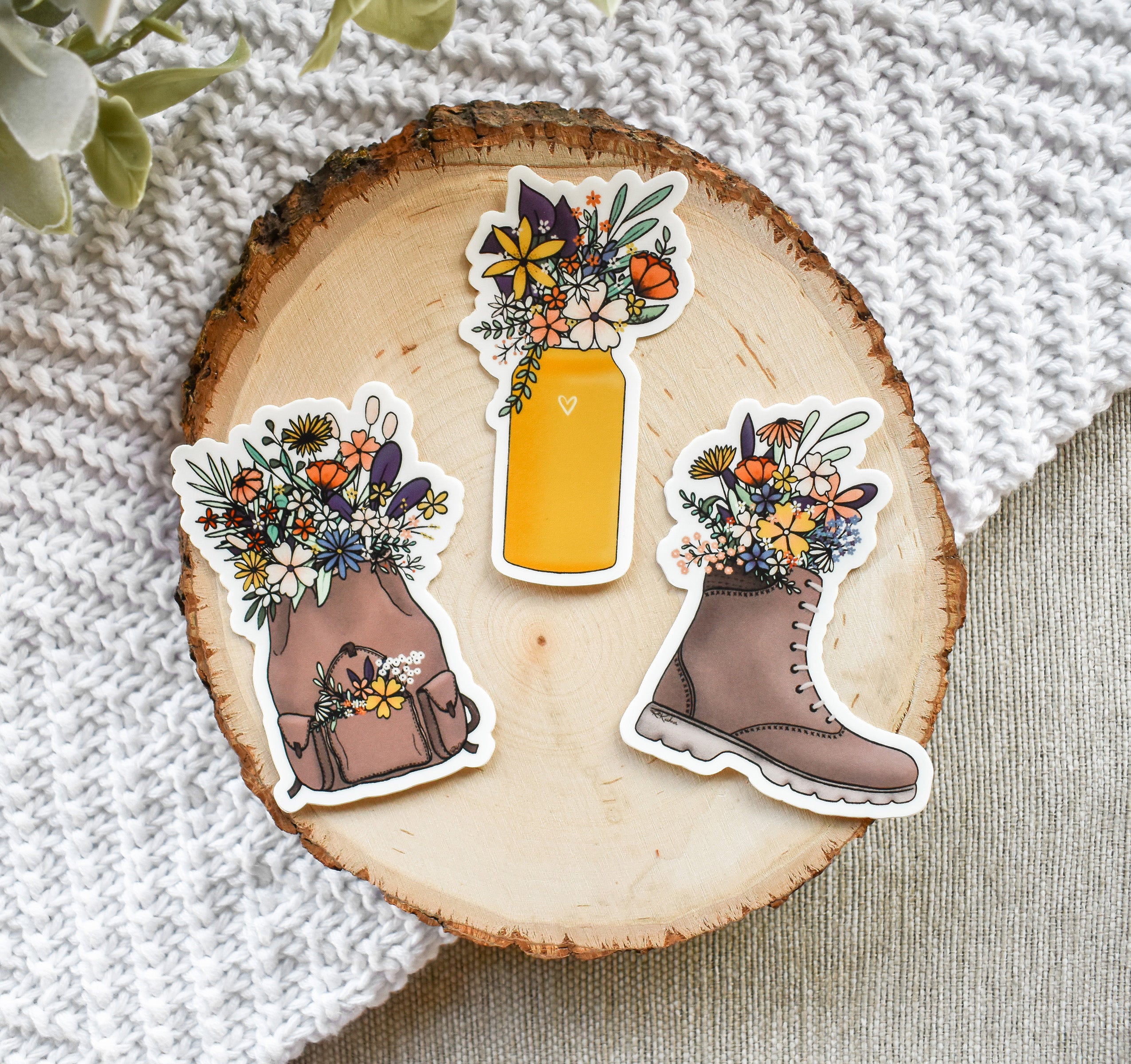 Outdoor adventure nature stickers - a set of three stickers featuring a hiking boot, water bottle, and backpack overflowing with beautiful wildflowers