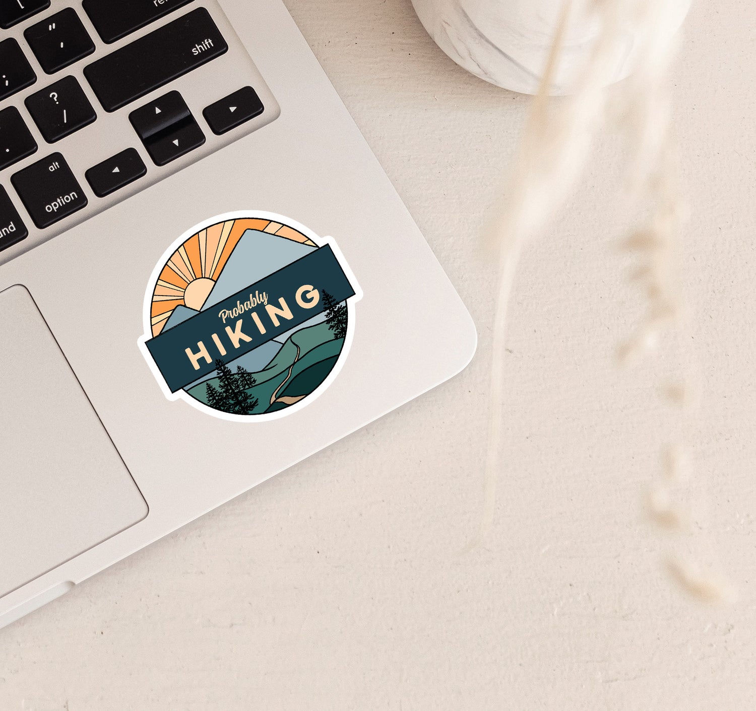 Mountain laptop sticker with a trail, pine trees, and a sunset with the phrase "probably hiking"