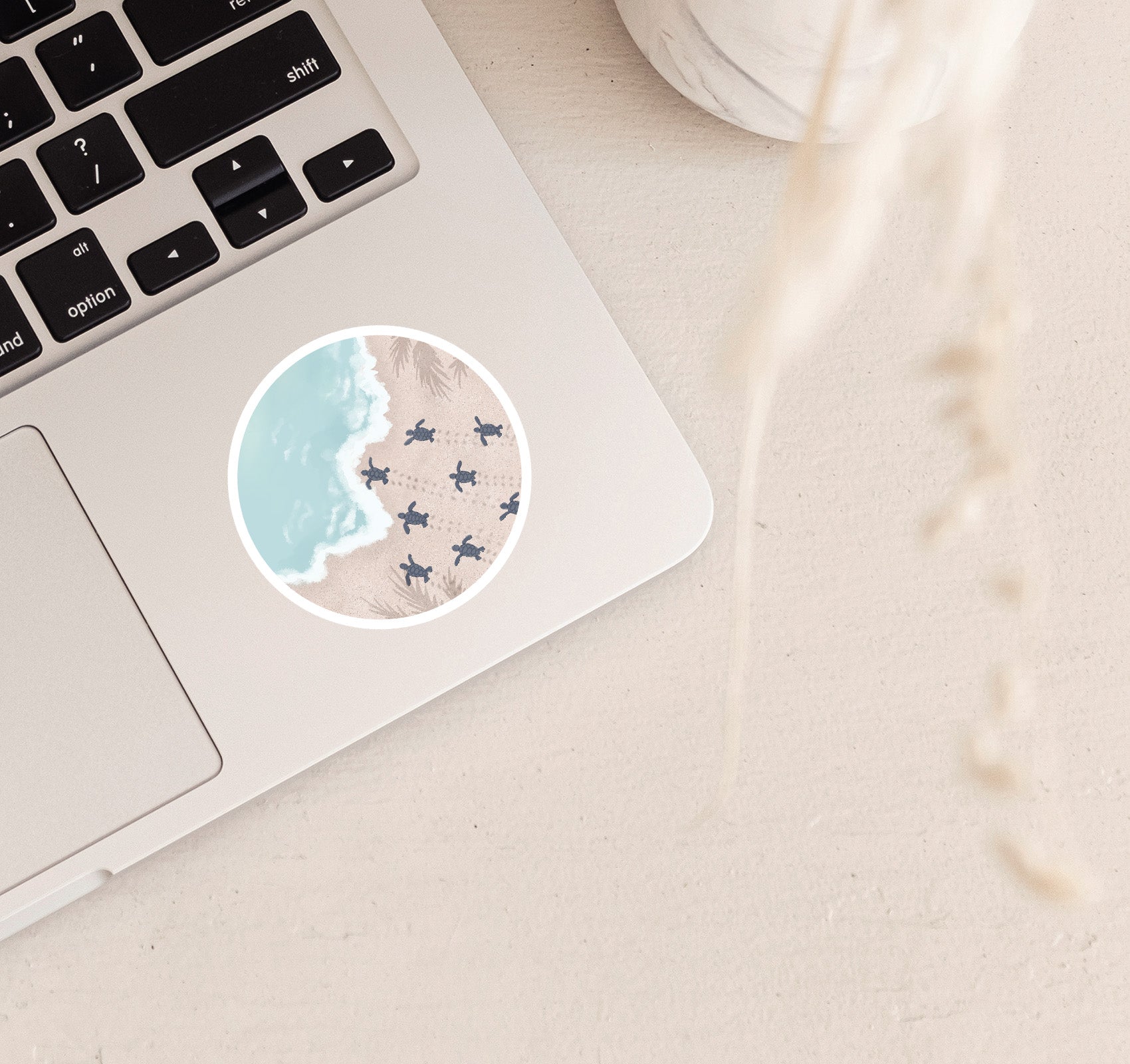 Round vinyl sticker on a laptop with baby sea turtles moving across the sand towards the ocean