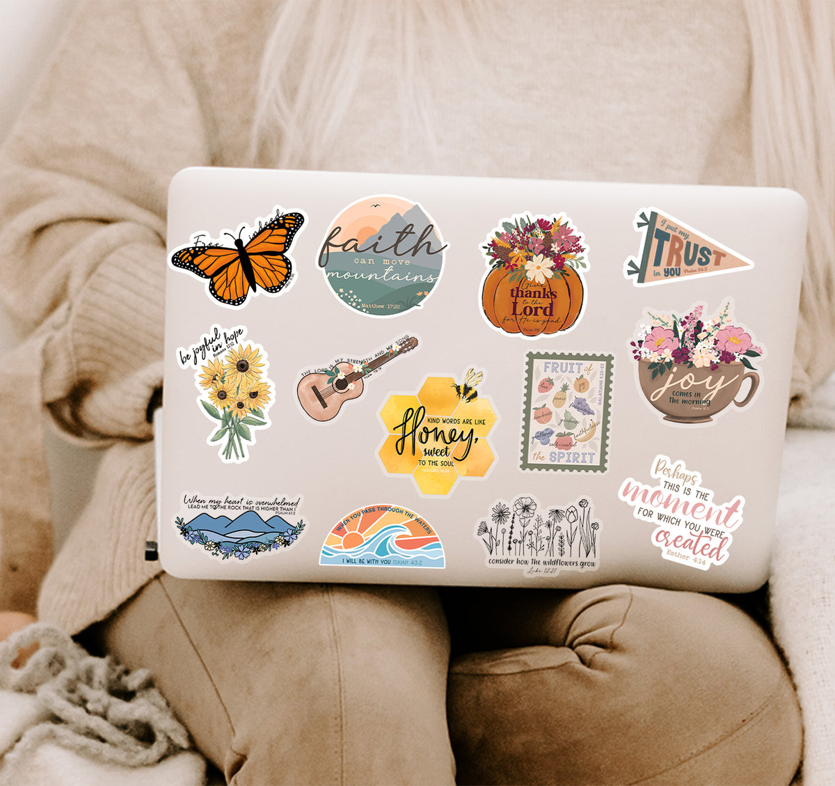 A silver laptop covered in colorful Christian faith stickers, resting on a person&