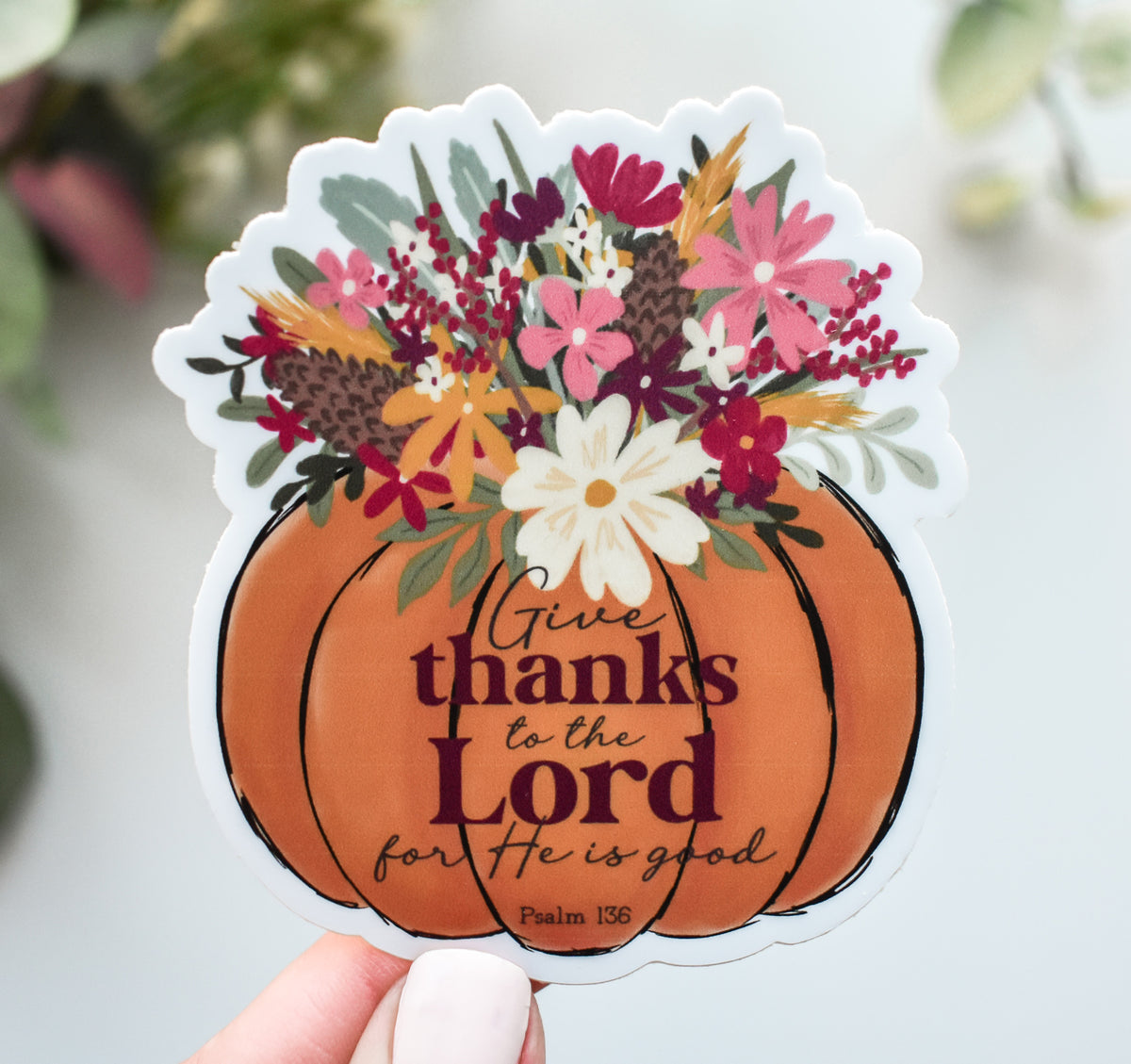 A die-cut sticker held by a hand, featuring an orange pumpkin with the text &