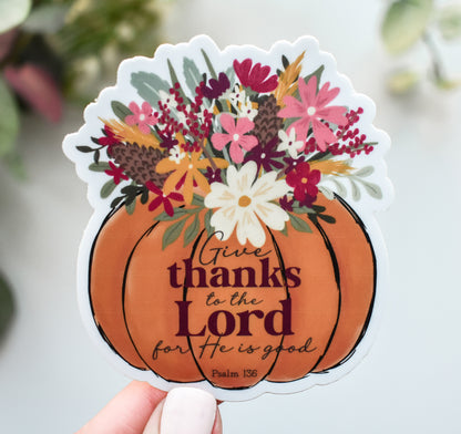 A die-cut sticker held by a hand, featuring an orange pumpkin with the text &