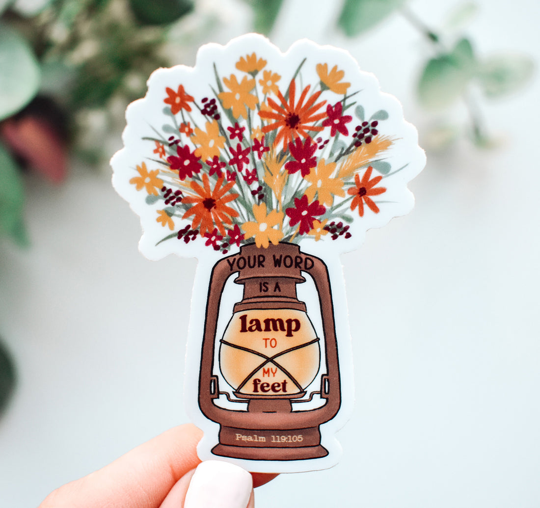 A scalloped die-cut Christian faith sticker held by a hand, featuring a brown lantern with the text &