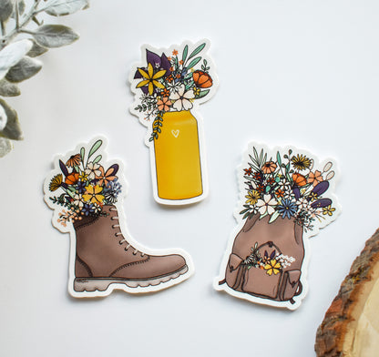 Outdoor adventure nature stickers - a set of three stickers featuring a hiking boot, water bottle, and backpack overflowing with beautiful wildflowers