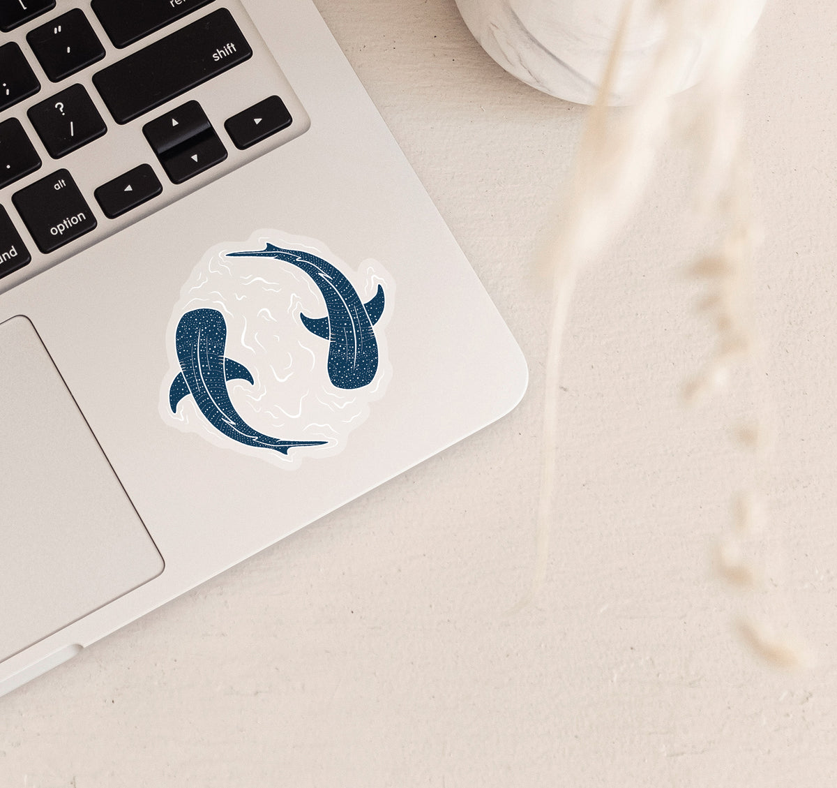 A clear vinyl sticker on a laptop of two whale sharks swimming in a circle with water lines surrounding them