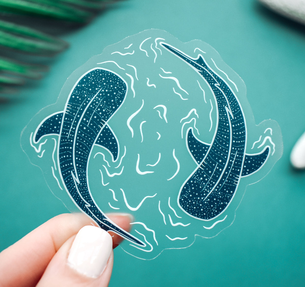 A clear vinyl sticker of two whale sharks swimming in a circle with water lines surrounding them