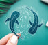 A clear vinyl sticker of two whale sharks swimming in a circle with water lines surrounding them
